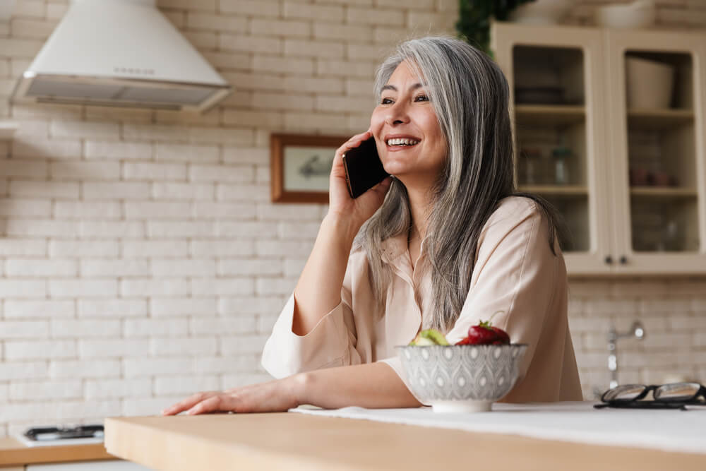 Older woman with long gray hair on the phone in kitchen